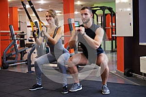 Slim woman with personal trainer working with battle ropes at gym