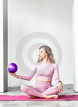 Slim woman with rubber ball rubber ball for rhythmic gymnastics. Training yoga in pink tight-fitting tracksuit in