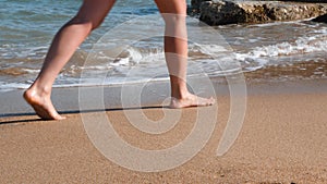 Slim woman`s legs walking on yellow sand along sea. Slim tanned legs on beach with sand. Young slim girl walks along sea and leave