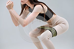 Slim woman in sportswear using rubber resistance band, doing exercise for glutes and legs