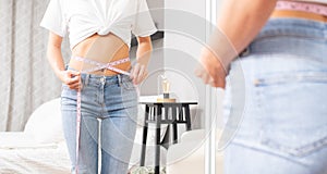 Slim woman standing in front of the mirror measuring her waist after weight loss