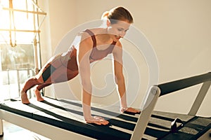 Slim woman wearing sports attire having anaerobic exercise on reformer