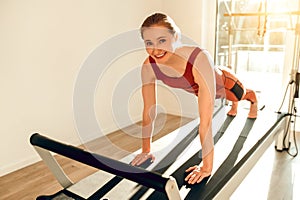 Slim woman wearing sports attire having anaerobic exercise on reformer