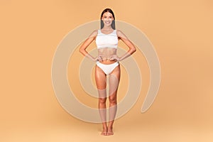 Slim woman in white underwear with perfect body shape and flat tummy posing over beige studio background, full length