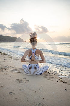 Slim yogi woman sitting in Padmasana  Lotus Pose on the beach. Hands in namaste mudra. View from back. Self care concept. Yoga