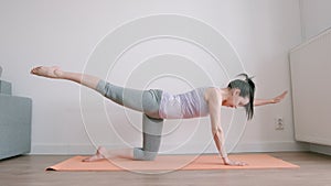 Slim young adult woman practising yoga on a mat at home