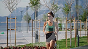 Slim young blonde woman jogging on promenade, city buildings on background. Sporty sexy woman running, exercising