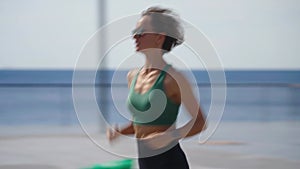 Slim young blonde woman jogging on promenade, city buildings on background. Sporty sexy woman running, exercising