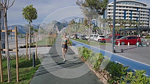 Slim young blonde woman jogging on promenade, city buildings on background. Sporty sexy woman running, exercising