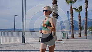 Slim young blonde woman jogging on promenade, city buildings on background. Sporty sexy woman running, exercising