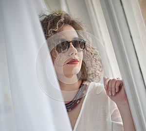 Slim young fashion model with curly hair wearing white blouse in a frame of window.