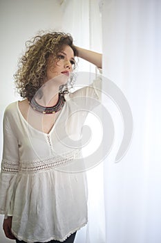 Slim young fashion model with curly hair wearing white blouse in a frame of window.