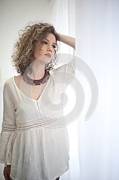 Slim young fashion model with curly hair wearing white blouse in a frame of window.