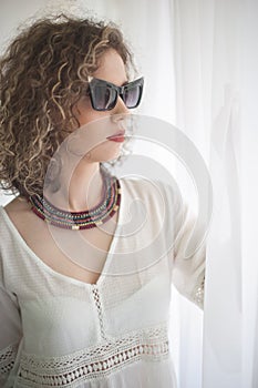 Slim young fashion model with curly hair wearing white blouse in a frame of window.