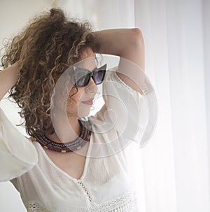 Slim young fashion model with curly hair wearing white blouse in a frame of window.