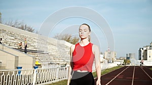 Slim young fitness runner with ponytail in sportswear walking on running track