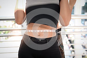 Slim young sport girl measuring her thin waist with tape measure, her exercise partner trainer helping her to measure her waist,