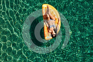 Slim young woman in bikini and sunglasses on the air mattress floats in the open sea