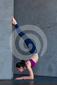 Slim young woman doing forearm stand or Peacock yoga pose against the wall