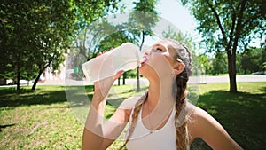 Slim young woman drinking water after training. Woman athlete takes a break, she drinking water, out on a run on a hot