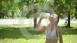 Slim young woman drinking water after training. Woman athlete takes a break, she drinking water, out on a run on a hot