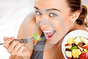 Slim young woman eating fruit salad