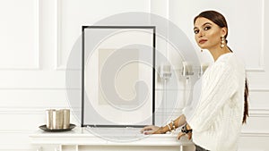 Slim young woman in luxury home interior. Picture frame, white wall. Space for advertising product and your decoration.