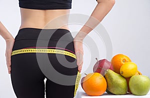 Slim young woman measuring her buttocks with a tape measure. In focus fruits for weight loss - apple, orange and pear.