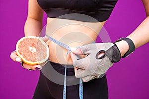 Slim young woman measuring her thin waist with a tape measure and with grapefruit