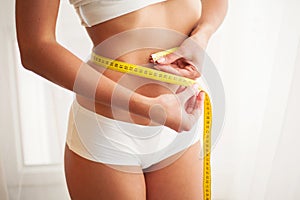 Slim young woman measuring her thin waist with a tape measure photo