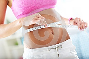 Slim young woman measuring her waist with a tape measure