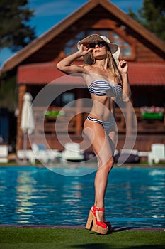 A slim young woman in swimwear at the poolside is standing straight and looking up.