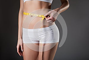 Slim young woman taking measurements of waistline