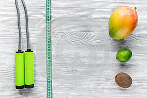 Slimming diet. Fruits mango, lime, kiwi and skipping rope on grey wooden table top view copyspace