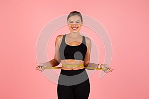Slimming and dieting. Smiling woman measuring her waist over pink studio background