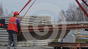 Slinger in helmet and vest supervises unloading at construction site. Real-time video. 4K resolution.