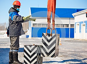 Slinger in helmet works outside. Signal to lift load up. Long workflow. Work of slinger in winter in open air during day photo