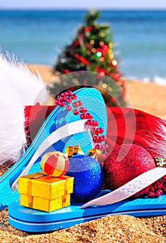 Slippers, christmas hat, gift box and new year tree on the seashore