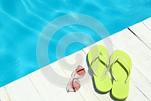 Slippers and sunglasses on wooden deck near swimming pool. Beach accessories