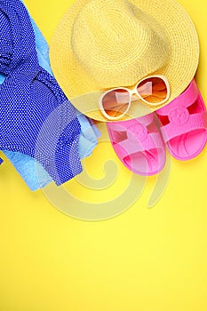 Slippers, swimsuit bikini, towel, hat and sunglasses on a pastel yellow background