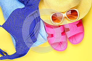 Slippers, swimsuit bikini, towel, hat and sunglasses on a pastel yellow background. Travel, sea, vacation, holiday.