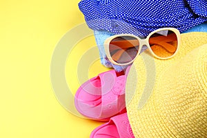 Slippers, swimsuit bikini, towel, hat and sunglasses on a pastel yellow background. Travel, sea, vacation, holiday.