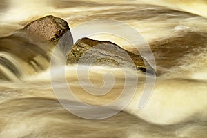 Slippery boulders in mountain stream. Clear water blurred by long exposure, low water level.