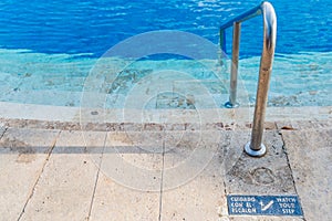 Slippery steps down to swimming pool with blue water and watch your step sign in both English and Spanish