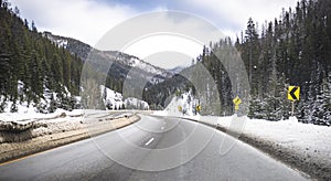 Slippery winding winter highway with heaps of snow on the side of the road after clearing the road and snow-covered mountains