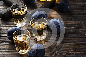 Slivovica - plum brandy or plum vodka, hard liquor, strong drink in glasses on old wooden table, fresh plums, copy space