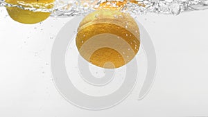 Slo-motion orange and lemon falling into water
