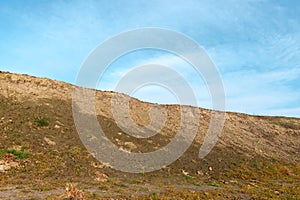 The slope of a clay hill against the backdrop of a beautiful blue sky. Lifeless soil. Sunny weather. Landscape