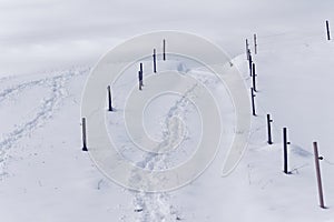 Slope with fence posts and traces in deep snow, white winter season