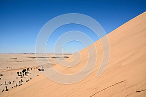The slope of a large dune in the desert. Below is a small place for parking and rest for tourists